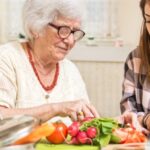 Grandmother and granddaughter preparing food together at kitchen.